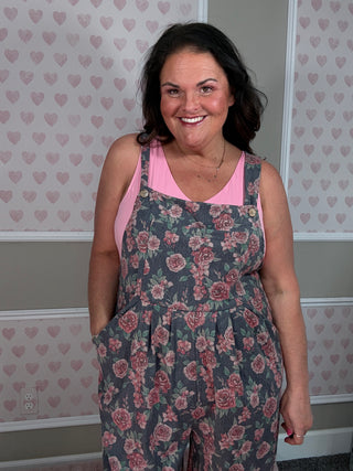 Woman wearing a floral overalls and pink top in a room with heart-patterned wallpaper.
