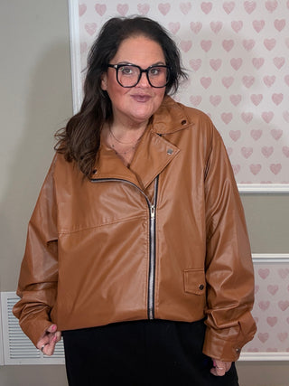 Person wearing a brown leather jacket in front of a wall with heart patterns.