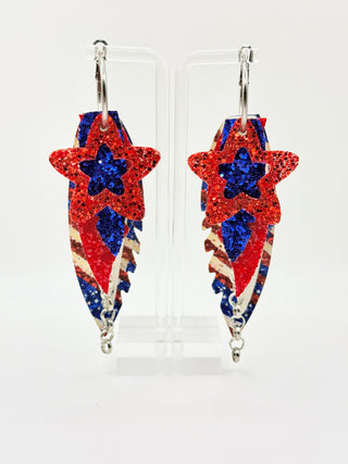 Star-shaped earrings with red, blue, and white design on a clear stand against a white background