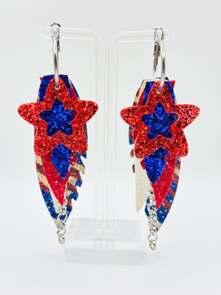 Star-shaped earrings with red, blue, and white design on a clear stand.