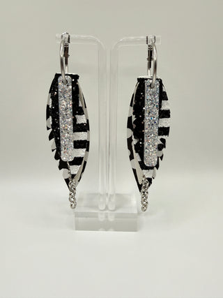 Black and white statement earrings with polka dot faux leather feather details, striped glitter accents, silver chain charm, and lightweight boutique design.