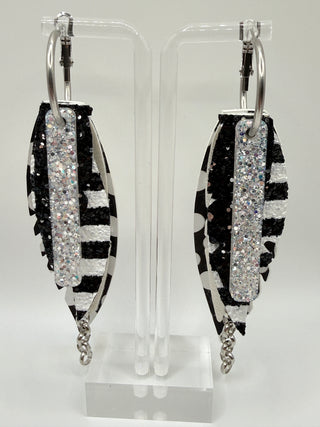 Black and white statement earrings with polka dot faux leather feather details, striped glitter accents, silver chain charm, and lightweight boutique design.
