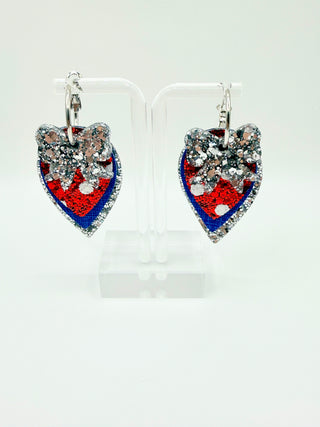 Layered patriotic statement earrings with silver glitter bow accent, silver glitter layer, royal blue textured faux leather, red glitter polka dot detail, and silver hoop closure.