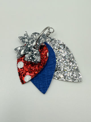 Layered patriotic statement earrings with silver glitter bow accent, silver glitter layer, royal blue textured faux leather, red glitter polka dot detail, and silver hoop closure.