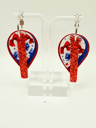 Layered patriotic statement earrings with red glitter accent, patriotic bow print, royal blue textured faux leather, red woven texture, and silver hoop closure.