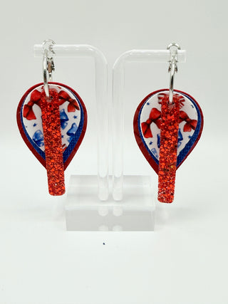 Layered patriotic statement earrings with red glitter accent, patriotic bow print, royal blue textured faux leather, red woven texture, and silver hoop closure.