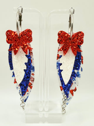 Patriotic bow print statement earrings with red and blue glitter accents, layered faux leather feather details, silver chain charm, and lightweight boutique design.