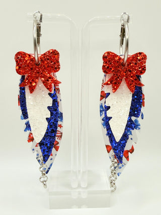 Patriotic bow print statement earrings with red and blue glitter accents, layered faux leather feather details, silver chain charm, and lightweight boutique design.