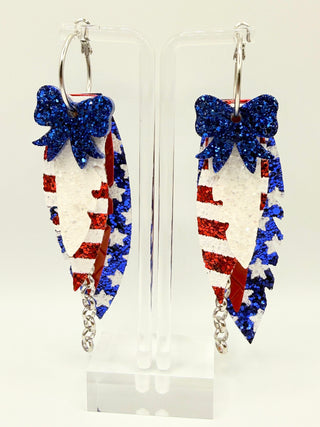 Patriotic red white and blue statement earrings with glitter star accents, layered faux leather feather details, silver chain charm, and lightweight boutique design.