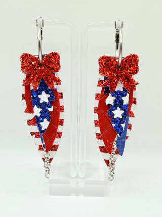 Patriotic red white and blue statement earrings with glitter stripes, star accents, layered faux leather feather details, silver chain charm, and lightweight boutique design.