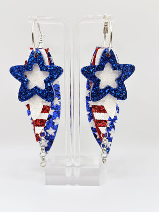 Star-shaped earrings with red, white, and blue design on a clear stand.