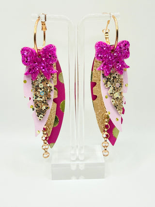 Pink and gold statement earrings with glitter bow accent, layered faux leather feather details, metallic polka dots, gold chain charm, and lightweight boutique design.