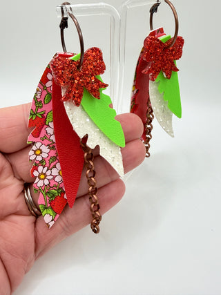 Red, pink, and green layered statement earrings with strawberry floral print, glitter bow accent, faux leather feather details, and bronze chain charm.