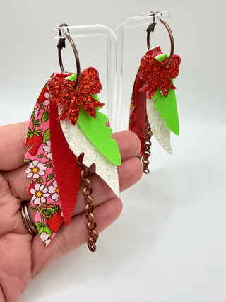 Red, pink, and green layered statement earrings with strawberry floral print, glitter bow accent, faux leather feather details, and bronze chain charm.