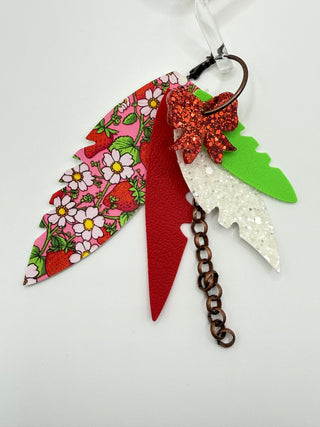 Red, pink, and green layered statement earrings with strawberry floral print, glitter bow accent, faux leather feather details, and bronze chain charm.