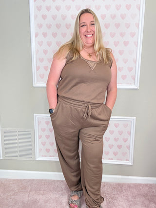 Person wearing a brown outfit standing in front of a wall with heart patterns.