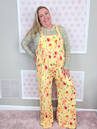 Woman wearing yellow floral overalls standing in front of heart wall.