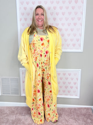Woman wearing a yellow floral jumpsuit against a white wall
