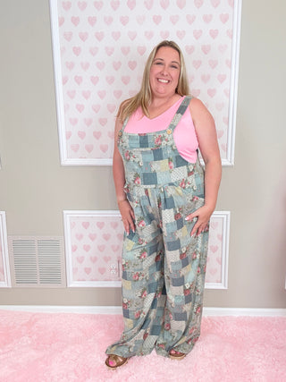 Person wearing a patchwork overalls in a room with pink walls and framed pictures.