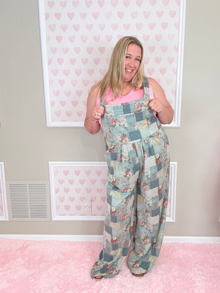 Person wearing a floral overalls standing in a room with pink walls and white frames.