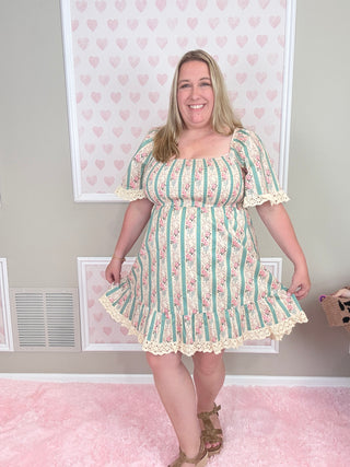 Woman wearing a floral dress standing in a room with pink walls and framed pictures.
