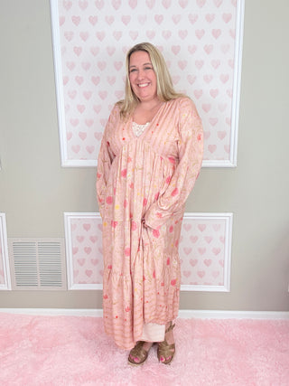 Woman wearing a pink floral dress standing in a room with pink walls and framed pictures.