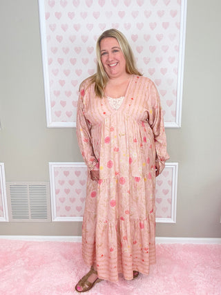 Woman wearing a pink floral dress standing in front of a wall with heart patterns.