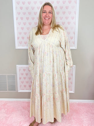 Woman wearing a long, light-colored dress standing against a pink wall with heart patterns.