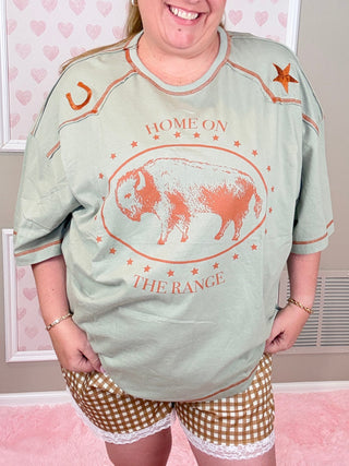 Person wearing a light green sweatshirt with a graphic design and checkered shorts in a room with heart-patterned wallpaper.