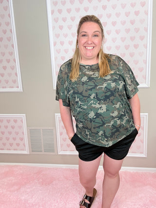 Person wearing a camouflage shirt in a room with pink walls and white frames.
