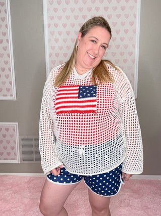 Person wearing a white mesh pullover with an American flag design, standing in a room with pink walls and a whiteboard.