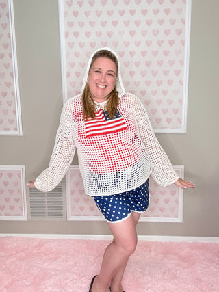 Person wearing a white patterned sweater and blue shorts in a room with pink walls and framed pictures.