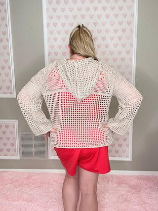 Person wearing a beige mesh top and red skirt in a room with pink walls and heart patterns.