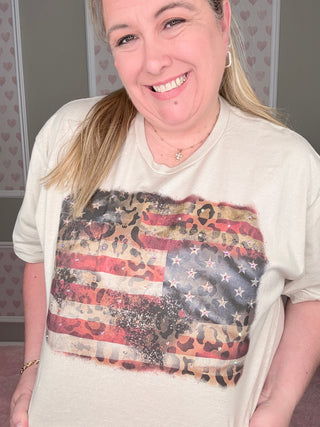 Woman wearing a natural shirt with a american flag and cheetah patterned design on a neutral background