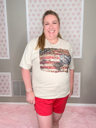 Woman wearing a natural shirt with a american flag and cheetah patterned design on a neutral background