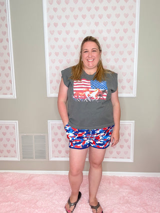 Person wearing a gray t-shirt with an American flag design and a colorful skirt in a room with heart-patterned wallpaper.