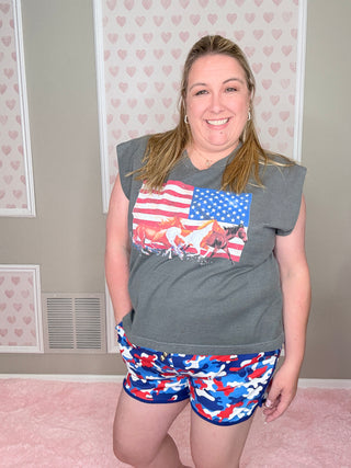 Person wearing a gray t-shirt with an American flag design and colorful shorts in a room with pink walls.
