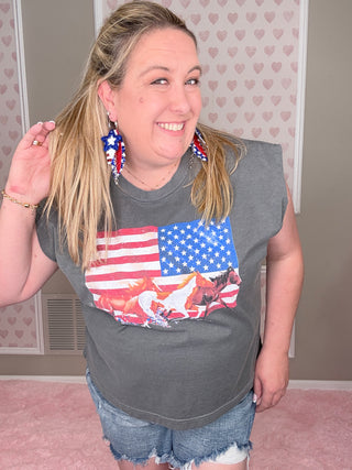 Person wearing a gray t-shirt with an American flag design, standing against a light-colored wall.