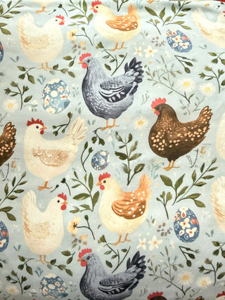 Patterned fabric with chickens, flowers, and leaves on a light blue background
