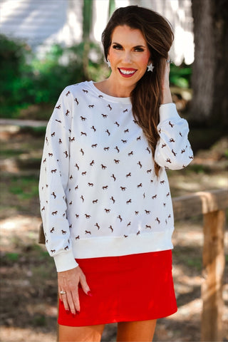 Woman wearing a white sweatshirt with horse pattern and red skirt outdoors.