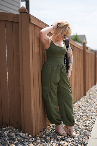 Person wearing a green romper standing on a gravel path with a wooden structure in the background.