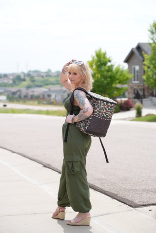 Person with a patterned bag walking on a sidewalk in army green romper. 