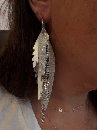 Close-up of a feather earring with rhinestones worn by a person.
