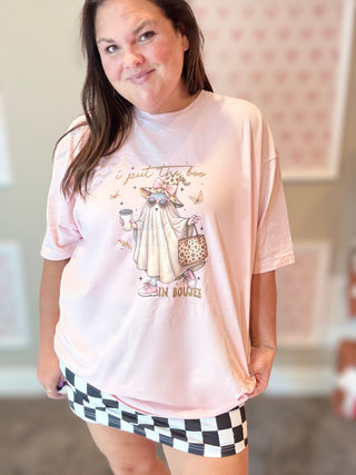 Woman wearing a light pink t-shirt with a graphic design and checkered shorts indoors.