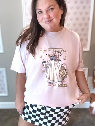 Person wearing a pink t-shirt with graphics and text, standing indoors.