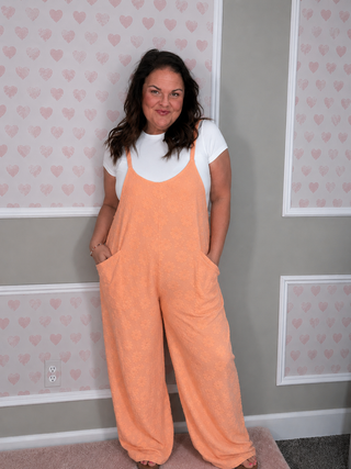 Peach daisy terry romper with adjustable straps, oversized pockets, and wide leg fit by Blakeley. 
