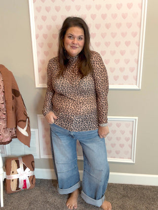 Woman wearing a leopard print top and blue jeans standing in a room with heart-patterned wallpaper.
