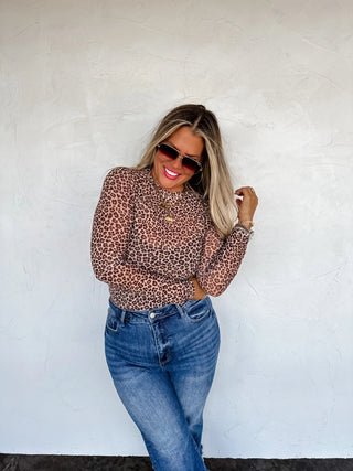 Woman wearing a cheetah mesh print top and blue jeans against a white wall
