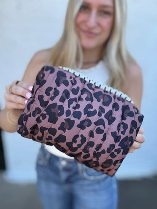 Person holding a leopard print clutch bag against a neutral background