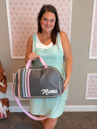 Woman carrying a gray Mama duffle bag with pastel stripes, styled with a pink graphic tank and pink bow skort.